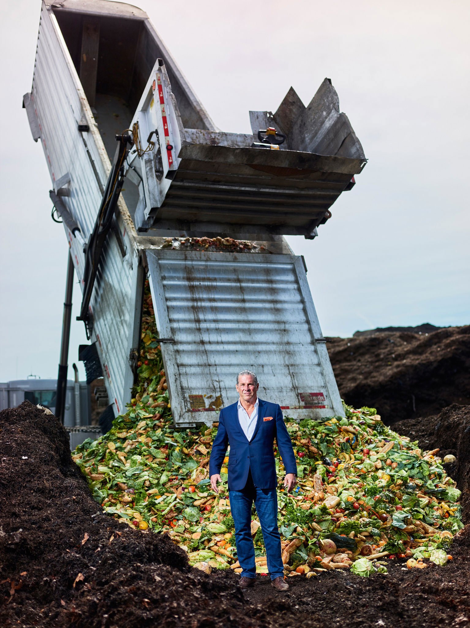 Charles Vigliotti on dirt hill in front of machine dumping compost