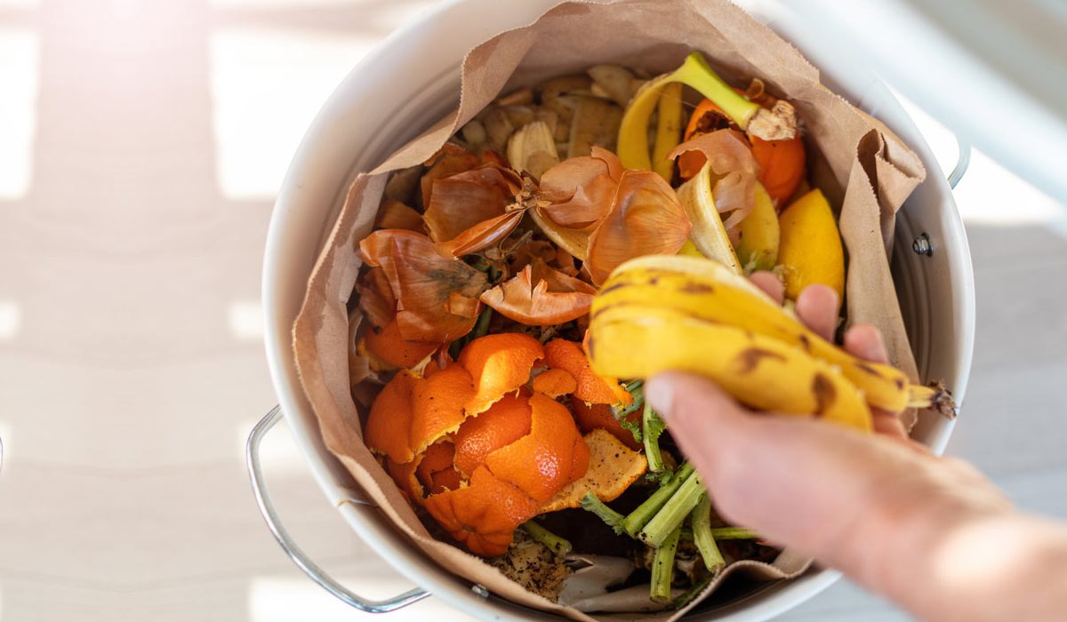 person tossing a banana peel into a garbage filled with food waste